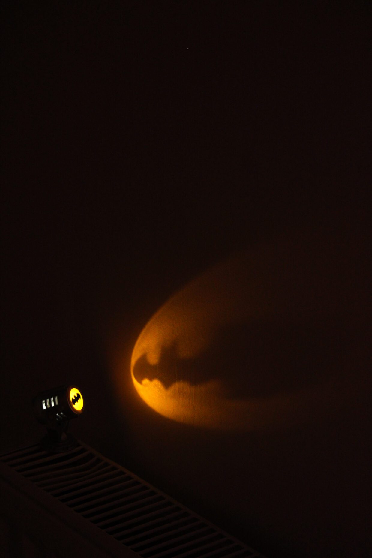 Miniature Bat-Signal projector casting a sharp Batman logo shadow on a dark wall in low light